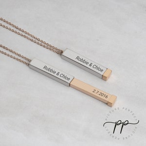 May include: Two personalized bar necklaces with gold-colored chains. The rectangular pendants are silver and gold-toned, engraved with names and a date. The text "Robbie & Chloe" is visible on both pendants.