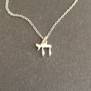 May include: A silver chain necklace with a small silver pendant in the shape of the Hebrew letter Chai.