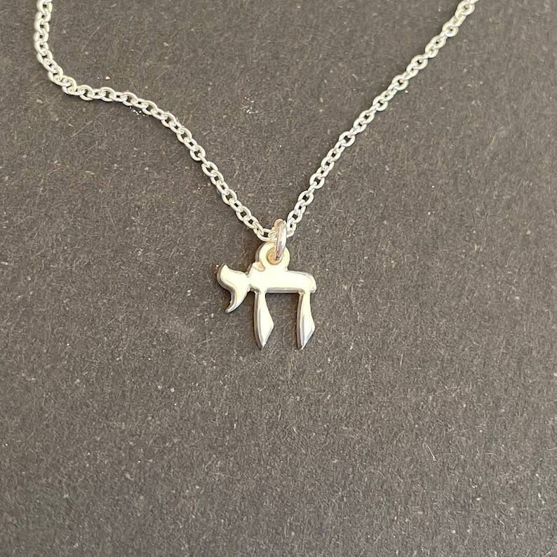 May include: A silver chain necklace with a small silver pendant in the shape of the Hebrew letter Chai.