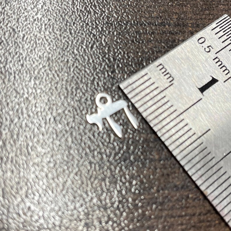 May include: A silver charm in the shape of the Hebrew letter "Heh" with a loop at the top for attaching to a chain or bracelet. The charm is approximately 1 cm in size.