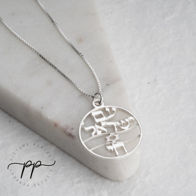 May include: A silver necklace with a round pendant featuring Hebrew text and a Star of David. The pendant is cut out, creating a delicate design.