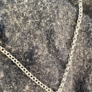 May include: A silver chain necklace on a dark gray fabric background.