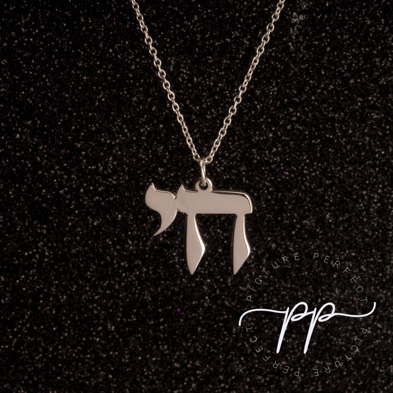 May include: A silver chain necklace with a pendant in the shape of the Hebrew letter Chai. The pendant is a simple, elegant design.