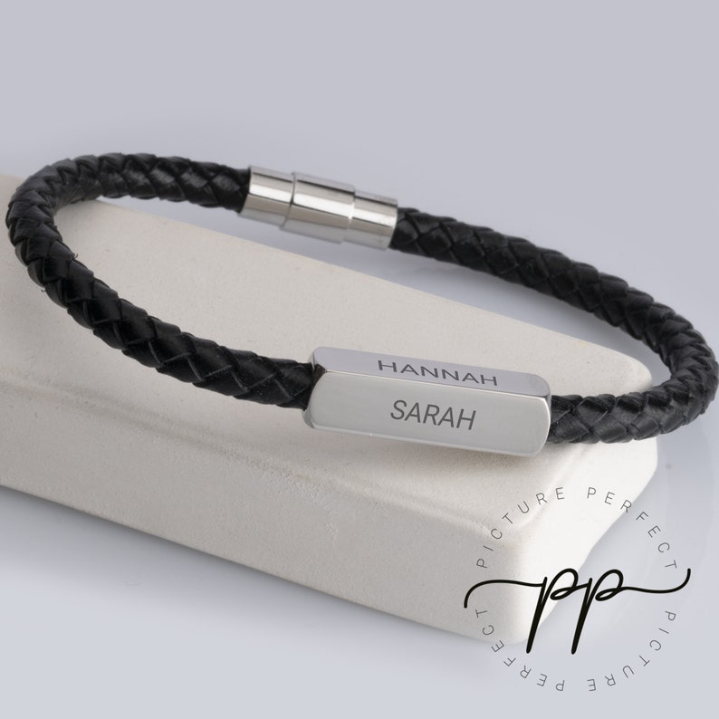 May include: Black leather bracelet with a silver bar engraved with the names "Hannah" and "Sarah".