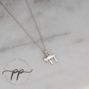 May include: A silver chain necklace with a small silver pendant in the shape of the Hebrew letter Chai.