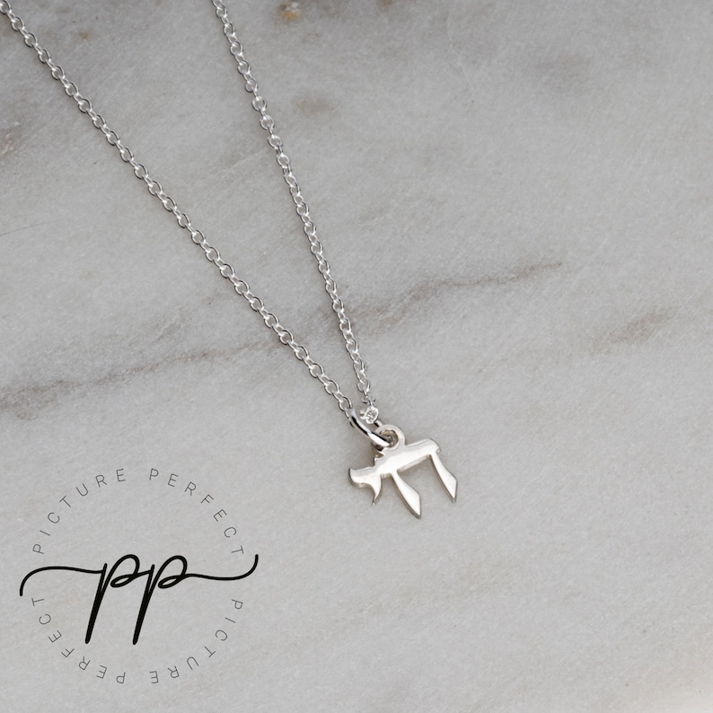 May include: A silver chain necklace with a small silver pendant in the shape of the Hebrew letter Chai.