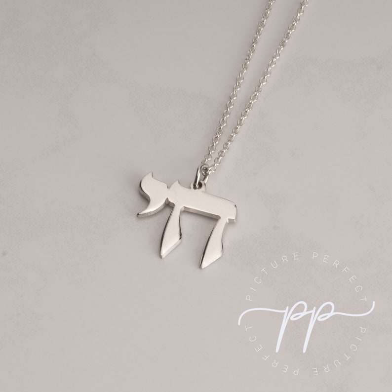 May include: A silver chain necklace with a silver pendant shaped like the Hebrew letter Chai. The pendant is on a white background.