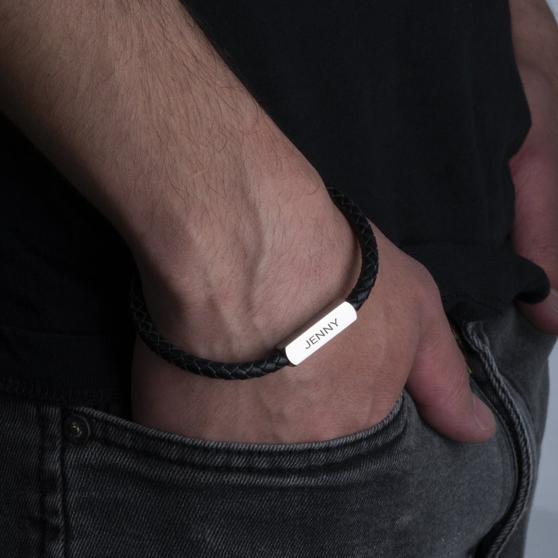 May include: A black leather bracelet with a silver plate engraved with the name "JENNY".