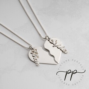 May include: Two silver necklaces with broken heart pendants. Each pendant has a name engraved on it: "Sophia" and "Olivia".
