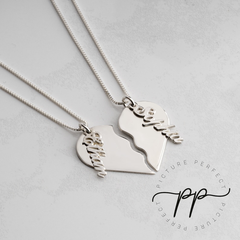 May include: Two silver necklaces with broken heart pendants. Each pendant has a name engraved on it: "Sophia" and "Olivia".
