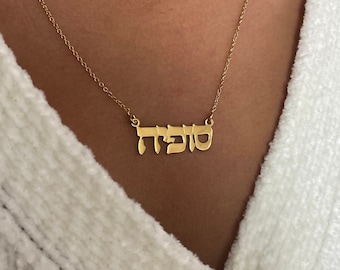 May include: A gold necklace with the Hebrew word "Shabbat" spelled out in a simple, modern font.