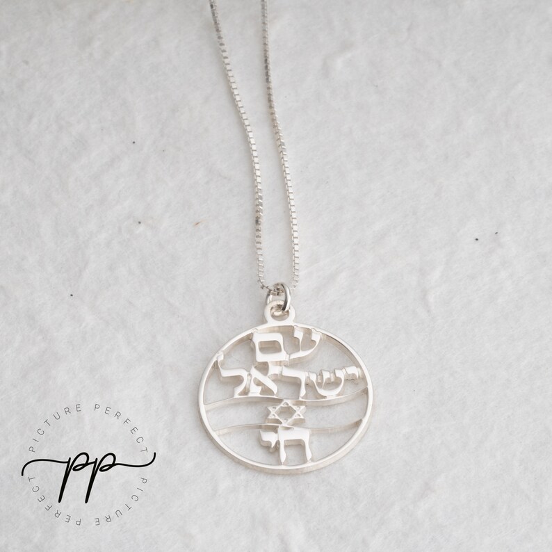May include: A silver necklace with a round pendant featuring Hebrew text and a Star of David. The pendant is cut out, creating a delicate design.
