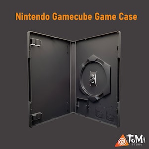Könnte beinhalten: Geöffnete, schwarze Nintendo Gamecube Spielhülle. Die Hülle ist leer und hat einen zentralen Disc-Halter. Der Text "Nintendo Gamecube Game Case" steht oben. Das ToMi Store-Logo befindet sich unten rechts.