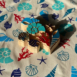 May include: A set of wooden stamps featuring various sea life designs, including seashells, starfish, coral, and fish. The stamps are painted in shades of blue, red, and white.
