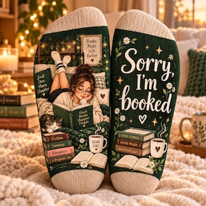 May include: A pair of dark green socks featuring a printed illustration of a person reading a book with a cat, alongside text that reads 'Books Make Life Better', 'Just One More Chapter', 'Good Books Happier People', 'Sorry, I'm booked', and 'Book Girl'.