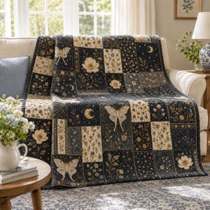 May include: A patchwork quilt featuring a dark navy blue and cream color palette. The fabric blocks display repeating patterns of moths, crescent moons, and various floral motifs. The quilt is stitched with a grid pattern across the surface.