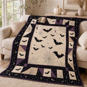 May include: A rectangular quilt featuring a cream-colored center panel with black bat silhouettes, spider webs, and small stars. The border consists of alternating black, purple, and cream geometric blocks decorated with bats and spider webs.