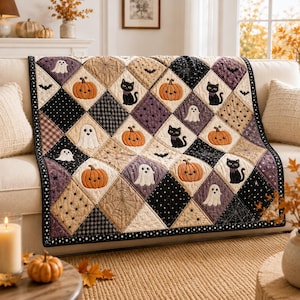 May include: A quilted throw blanket featuring a diamond-patterned design with alternating squares of black, purple, and beige. The fabric displays embroidered motifs of orange pumpkins, black cats, white ghosts, bats, and spiderwebs.