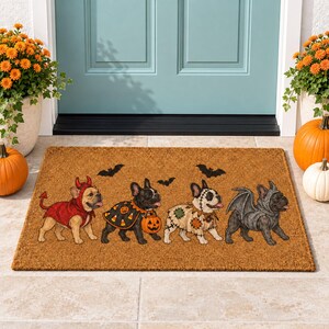 May include: A rectangular tan coir doormat featuring four French bulldogs in Halloween costumes. The dogs are dressed as a devil, a candy corn collector, a Frankenstein monster, and a bat. Three black bats are printed above the dogs.