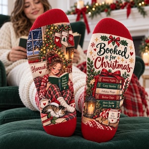 May include: A pair of red and white holiday-themed socks featuring a graphic of a person reading a book with a cat, a Christmas tree, and stockings. The text reads Booked for Christmas, Snowy Nights, Cozy Stories, Holiday Magic, and Hot Books.
