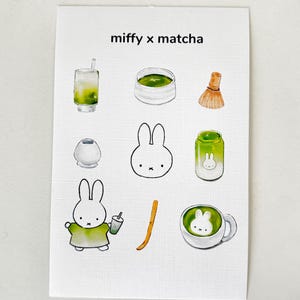 Op de afbeelding: Een witte kaart met de tekst "miffy x matcha" en illustraties van matcha-gerelateerde items. Deze omvatten een matcha-drankje, een kom matcha, een garde, een kleine container, een Miffy-konijn, een pot en een kopje matcha.