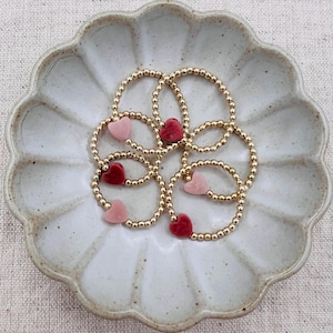 May include: A set of six gold beaded rings with heart-shaped charms. The charms are alternating pink and red.