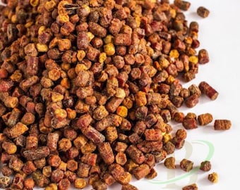 May include: A pile of bee pollen granules featuring a variety of textures and shapes in shades of deep reddish-brown, golden yellow, and burnt orange. The small, cylindrical pellets are clustered together, creating a dense, granular mound.