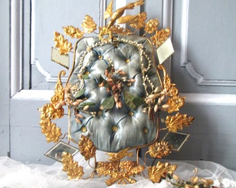 May include: A vintage blue satin pillow with gold trim and a bird design, surrounded by gold leaf branches and mirrors. The pillow is decorated with pearl beads and dried flowers.