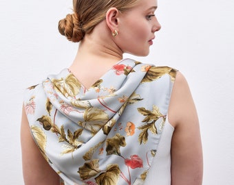 May include: A light blue silk scarf with a botanical print featuring large brown and tan leaves, and red and orange flowers. The scarf is draped over the shoulders.