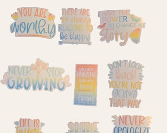 Puede incluir: Nueve pegatinas coloridas con citas inspiradoras. Las pegatinas presentan un fondo degradado arcoíris con texto blanco. Las citas incluyen "You are worthy", "There are so many reasons to be happy", "I have the power to change my story", "Never stop growing", "You are amazing, you are brave, you are strong", "Don't look back, you're not going that way", "Life is tough but so are you", "Shine like the stars", and "Never apologize for being you".
