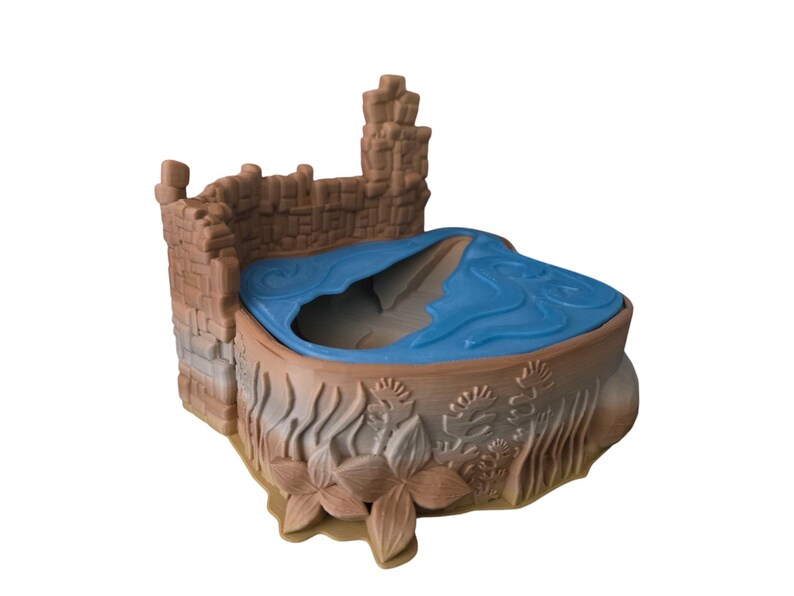 K&ouml;nnte beinhalten: Ein braunes Plastikspielzeugschloss mit einem blauen Plastikpool in der Mitte. Das Schloss hat eine Mauer aus braunen Steinen und einen Turm auf der linken Seite. Der Pool ist von braunen Plastikpflanzen und Blumen umgeben.