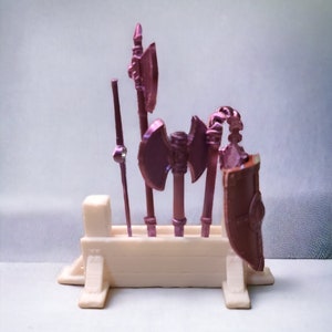 May include: A set of five miniature fantasy weapons, including axes and a spear, displayed on a white wooden stand. The weapons are painted in a metallic pink color.