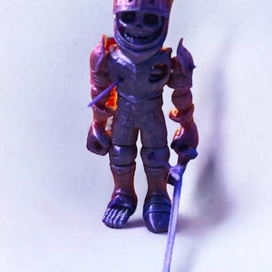 May include: A small, purple and orange plastic toy knight figurine with a sword. The knight has a skeletal face and is wearing armor.