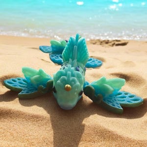 May include: A blue and green 3D printed sea creature with a gold accent on a sandy beach.