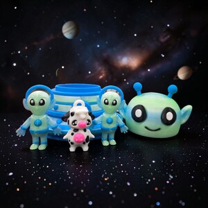 May include: A collection of colorful 3D-printed alien figurines and a cow figurine. The aliens are green and blue, with large eyes and helmets. The cow is white with black spots and a pink nose. A blue and white spaceship is in the background.