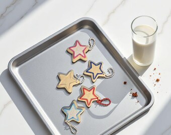 Könnte beinhalten: Eine Sammlung sternförmiger Schlüsselanhänger mit farbigen Akzenten, darunter Rot, Blau und Rosa, liegt auf einem silbernen Tablett. Ein Glas Milch steht daneben. Die Schlüsselanhänger haben silberne Kettenbefestigungen.