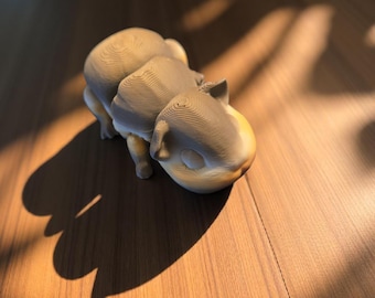 Könnte beinhalten: Eine 3D-gedruckte Skulptur eines stilisierten Tieres, möglicherweise eines Nilpferds oder einer ähnlichen Kreatur, in Grau- und Beigetönen. Die Skulptur hat ein geschichtetes, strukturiertes Aussehen und befindet sich auf einer Holzoberfläche mit Schatten.