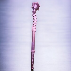 May include: A pink metal spiked ball on a chain attached to a long, thin, pink metal rod.