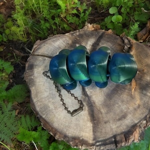 Puede incluir: Una cadena de plástico azul y verde con una cadena de metal unida. La cadena está sobre un tocón de árbol.