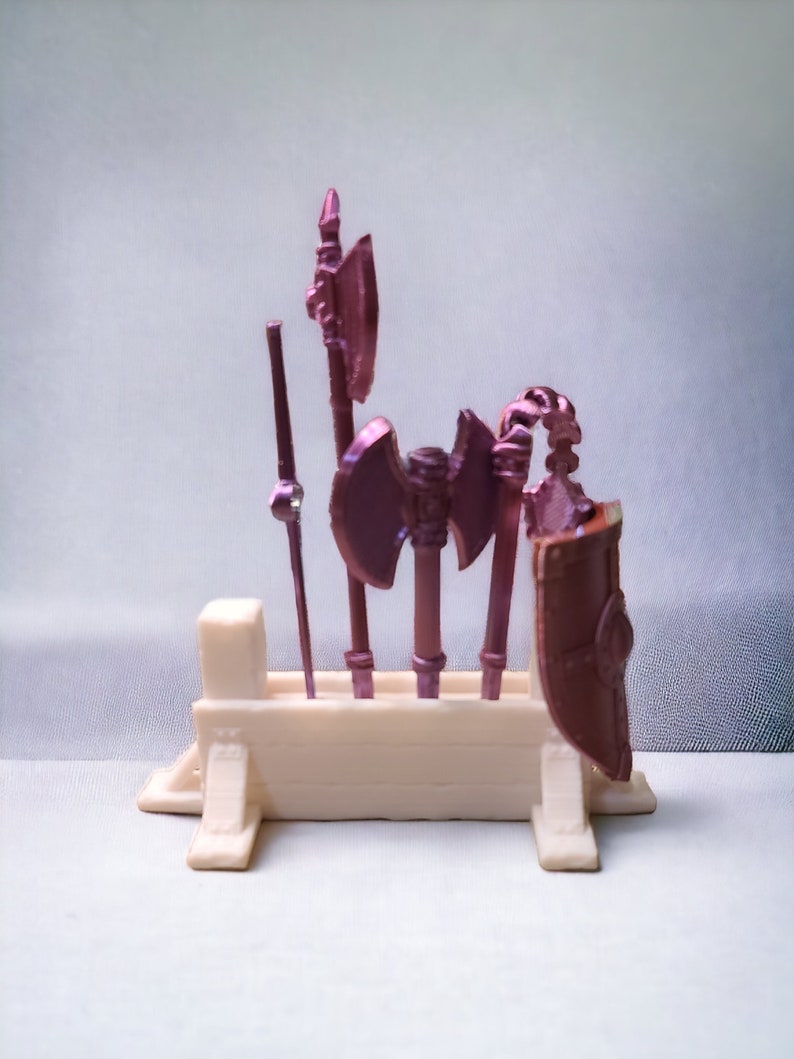May include: A set of five miniature fantasy weapons, including axes and a spear, displayed on a white wooden stand. The weapons are painted in a metallic pink color.