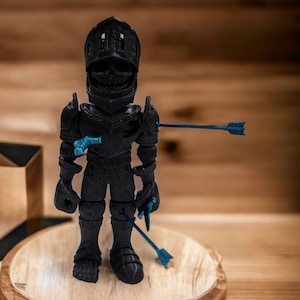May include: A black 3D printed figurine of a knight wearing armor and a helmet. The knight is pierced by several blue arrows. The figurine is standing on a wooden base.