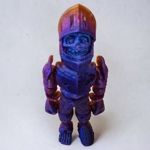 May include: A small, 3D printed figurine of a knight wearing armor. The figurine is painted in a gradient of purple and blue, with a gold helmet. The knight is standing with its arms at its sides.