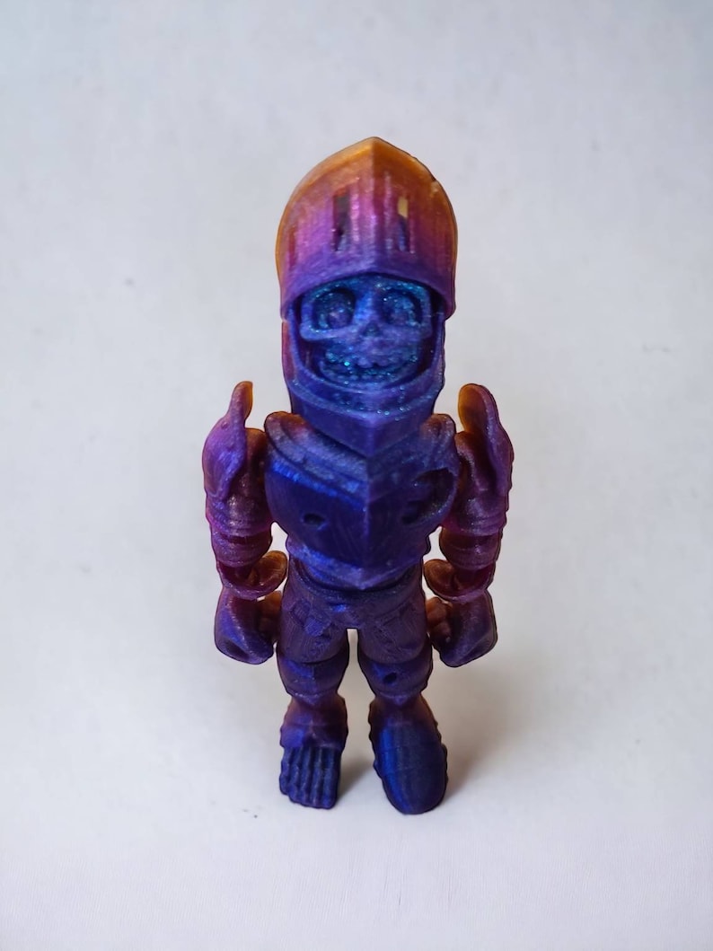 May include: A small, 3D printed figurine of a knight wearing armor. The figurine is painted in a gradient of purple and blue, with a gold helmet. The knight is standing with its arms at its sides.