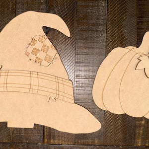 May include: Two unfinished wooden cutouts: a witch's hat with a plaid band and a patch, and a pumpkin with a stem and leaves. The hat is on the left, and the pumpkin is on the right. Both are unpainted.