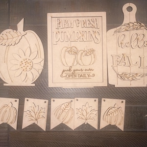May include: Wooden craft cutouts for fall decor.  The set includes a pumpkin, a sign that says "Farm Fresh Pumpkins, pick your own, open daily", a sign that says "hello fall", and a banner with five flags.  The flags have images of pumpkins and leaves.