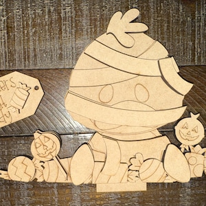 May include: A wooden cutout of a mummy duck with candy and jack-o'-lanterns. The mummy duck is surrounded by Halloween-themed candies and pumpkins. A tag with the words "quackers about candy" is also included.