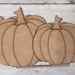 May include: Three unfinished wooden pumpkins with leaf accents. The pumpkins are stacked on top of each other and are ready to be painted.