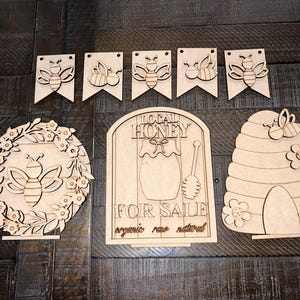 May include: Wooden craft kit for making a honey bee themed sign. The kit includes a sign that says "Local Honey For Sale Organic Raw Natural", a beehive, and several bee banners.