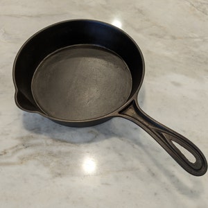 May include: A black cast iron skillet with a long handle. The skillet is empty and has a smooth surface.