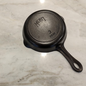 May include: A black cast iron skillet with a handle. The skillet is labeled "MERIT 3 1501".